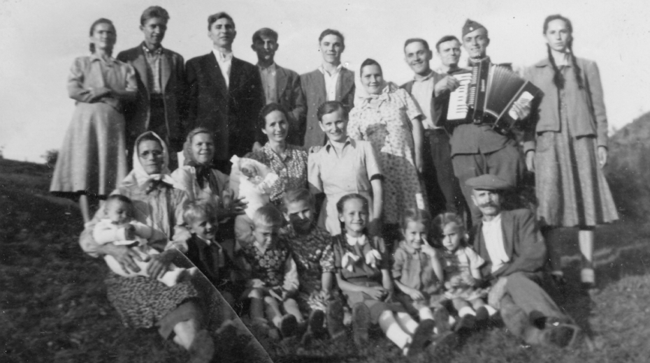 Hromadná fotografie několika deportovaných rodin z Eibentálu: Nedvědovi, Šrámkovi, Fiklovi a Jágrovi. Anna Urban sedí v dolní řadě s copánky uprostřed. Comanesti, první polovina 50. let. Zdroj: archiv pamětnice