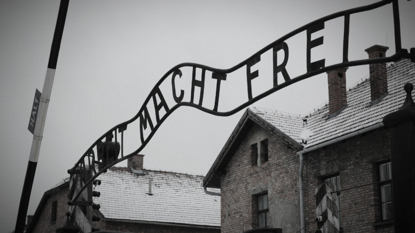 Vstupní brána do tábora s nápisem „Arbeit macht frei“, který byl umístěn na branách mnoha nacistických koncentračních táborů jako cynické prohlášení, že sebeobětování otrockou prací může přinést duševní svobodu. Zdroj: Wikimedia Commons
