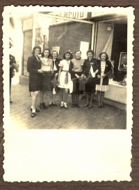 Po osvobození (uprostřed) v roce 1945. Rodina stojí před jejich domem, v rukou drží sovětské vlaječky, ušité doma maminkou pamětnice, ve výloze je vidět portrét prezidenta E. Beneše.