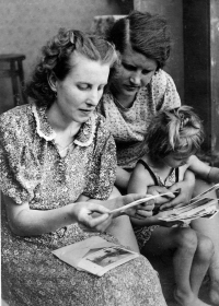 Milada is sitting on the lap of aunt Löschová, along with her mother Julie Světelská, they are looking at photographs. 1940