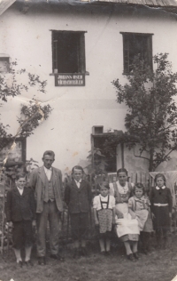 Rodina Oser (zleva Johann ml., tatínek Johann, Hermann, Emma, maminka Johanna, Helge, Mathilde) před svým domem v Huťském Dvoře na Šumavě. Na domě nápis "Johann Oser Viehverteiler", 1944