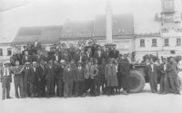 A group photo of new tractor drivers. They successfully passed a driving test and Jiří Boháč therefore could work not only as an auxiliary worker but as a proper tractor driver in the machine tractor station in Malče. The square in Chotěboř in May 1949. Jiři Boháč wearing a black jacket is on the right in the second row just behind the tractor wheels