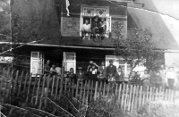 Ladislav Gavlas (na ramenou staršího bratra Antonína) před rodnou chalupou, v okně rodiče Pavel (v německé uniformě železničáře) a Johana, Mosty u Jablunkova - Filůvka, cca 1939
