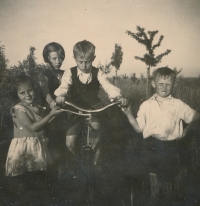 At her aunt and uncle's house in Karlovice, the future bishop Josef Koukl (1926-2010) is sitting on a bicycle, next to him are his siblings Líba and Dáda. The aunt and uncle had an apartment on the first floor of the Koukola's villa (the villa of Rudolf Koukola - the Prague arcitect's villa in Prague 6 - Bubenč at the corner of Pelléova and Slavíčkova streets)