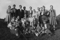 A group photo of several deported families from Eibentál: Nedvěd, Šrámek, Fikl and Jágr. The following came to visit them: František Fikl's half-brother with his wife (standing together on the left), Viktor Fikl (with accordion) and Kristýna Fiklová's sister (standing on the far right). Anna sits in the middle with her braids and her sister Margareta next to her. In the right corner sits grandfather Josef Fikl, who died in Comanesti. Comanesti - Romania, first half of the 1950s
