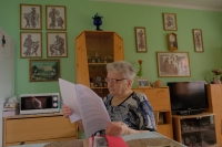 Stylizovaný portrét Drahomíry Starobové v jejím bytě, v pozadí obrázky, které ručně vyšívala