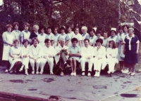 Kolektiv zdravotních sester. Manželka Jiřího Jaroše jako vrchní sestra očního oddělení sedí uprostřed v modrých sesterských šatech, vedle ní primář oddělení, doktor Štefek. Mezi lékaři doktorka Janovská, 70. léta 20. století