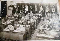 1. třída. v první lavici z leva Evička Platovská, která se nevrátila z koncentráku. Pamětnice vzadu v uličce podává křídu